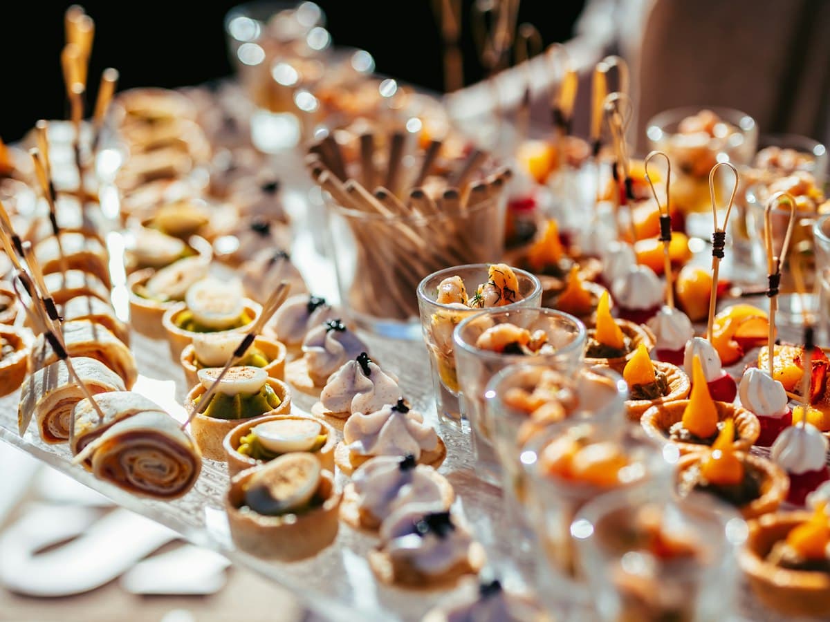 A catered table laid with canapés, filled tartlets, shrimp shot glasses and skewered bites, ready for guests