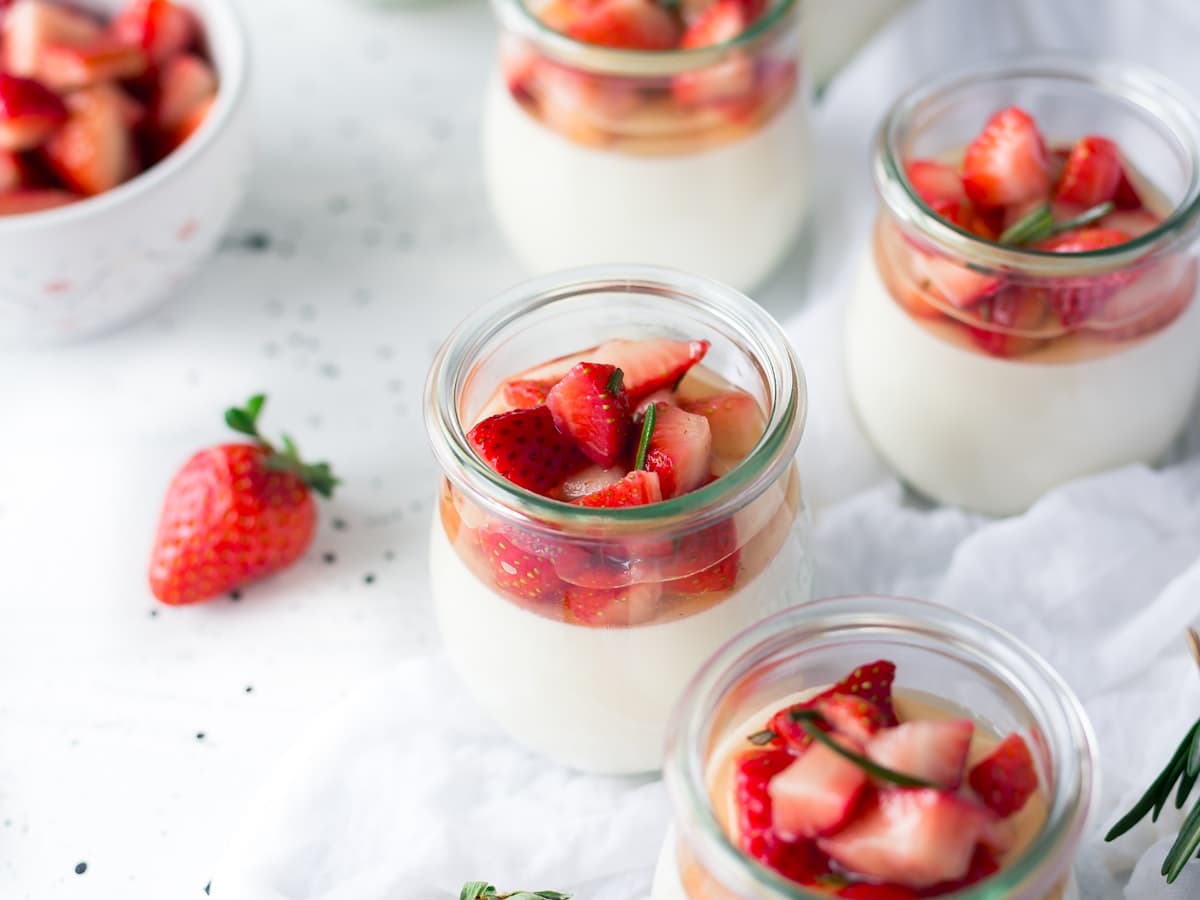 Small glass jars of panna cotta topped with chopped strawberries, with fresh strawberries alongside