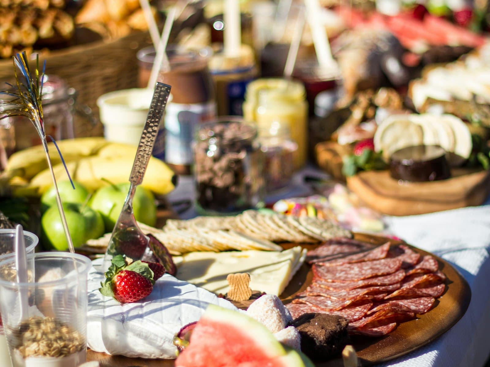 An outdoor grazing table laid with a charcuterie board, cured meats, cheeses, crackers, fresh fruit and jars of preserves